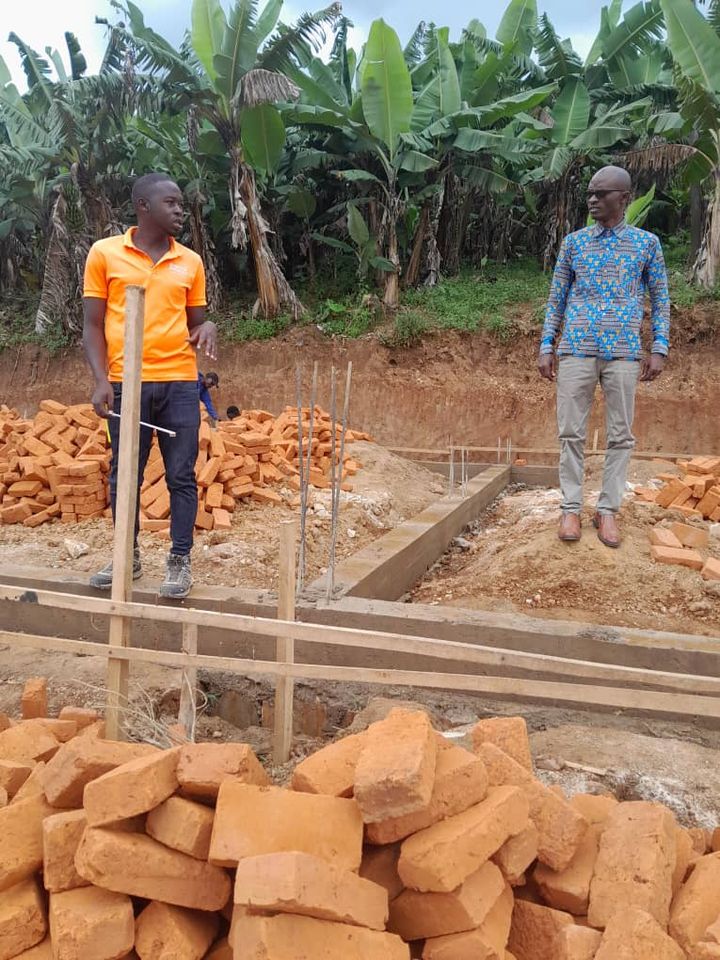 Zwei Männer der Bauleitung am Fundament, vorne ein Ziegelstapel