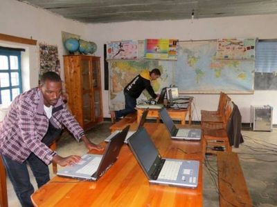 Zwei Männer richten Laptops auf Holztischen in einem Klassenraum ein